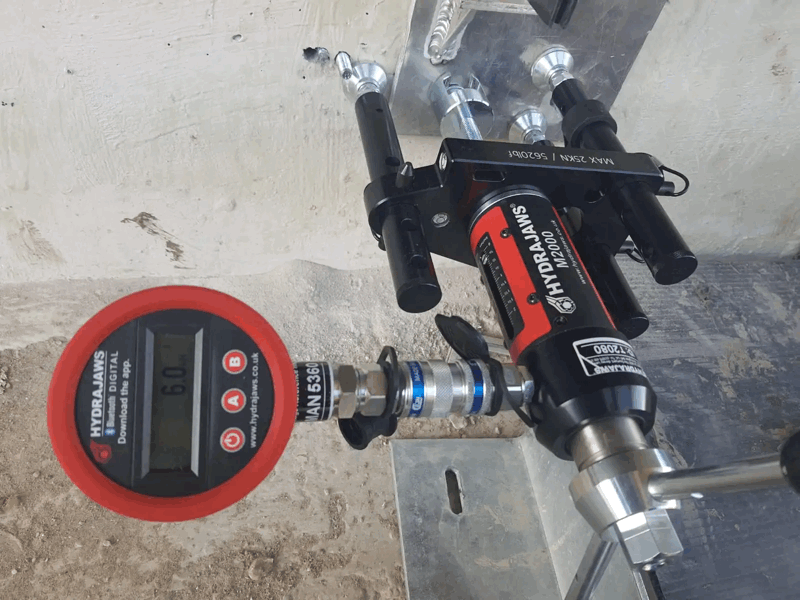 Cladding Pull Out Testing With Hydrajaws Digital Gauge Red Hydrajaws digital gauge attached to a pull-out testing rig on a concrete facade anchor