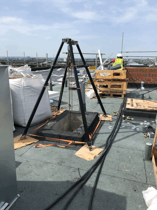 Black tripod rig set up over a roof access hatch for cladding pull out testing with orange straps and safety cables