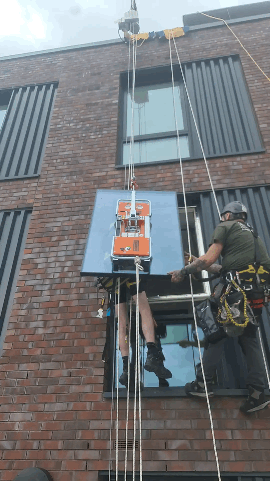 Cladding Pull Out Testing via Rope Access on Building Facade Rope access technician conducts cladding pull out testing with orange equipment rig on a brick and dark panel facade