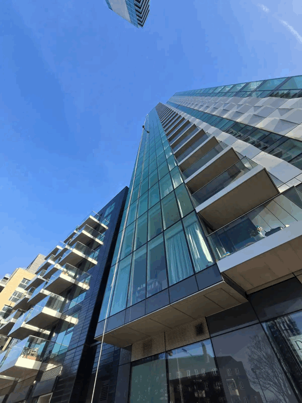 Angular glass-clad residential tower with balconies rising against a clear blue sky