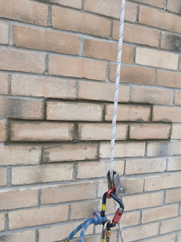 Rope access line with carabiners hangs against a brick cladding wall during a cladding inspection