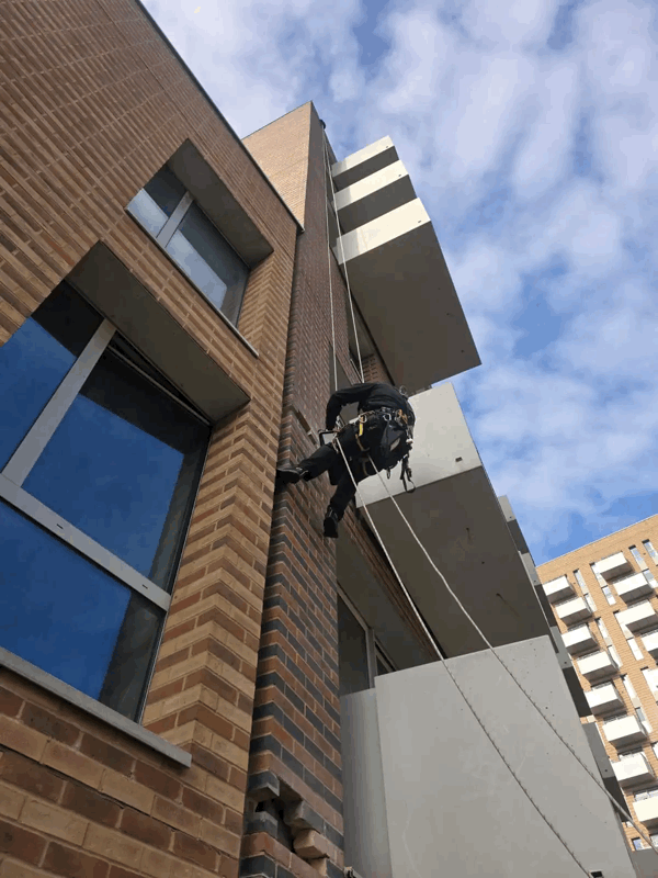 Rope access technician abseiling down a brick-clad building facade during a cladding inspection