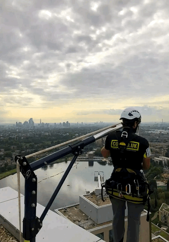 Rope access technician in helmet and harness inspects high-rise building facade above London skyline