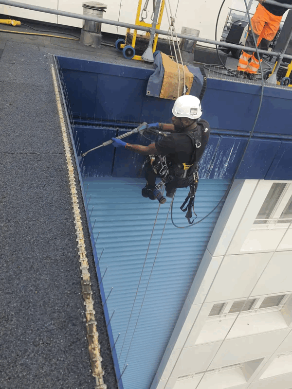 Rope access technician in harness inspecting blue metal cladding panels on a high-rise building facade