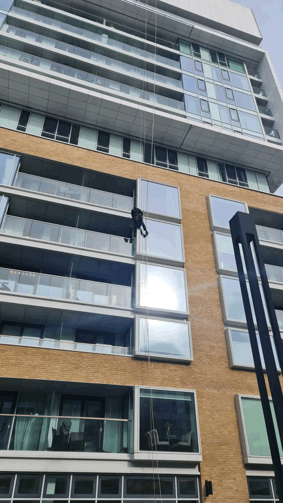 Rope access technician abseiling down a brick-clad high-rise building during a cladding inspection