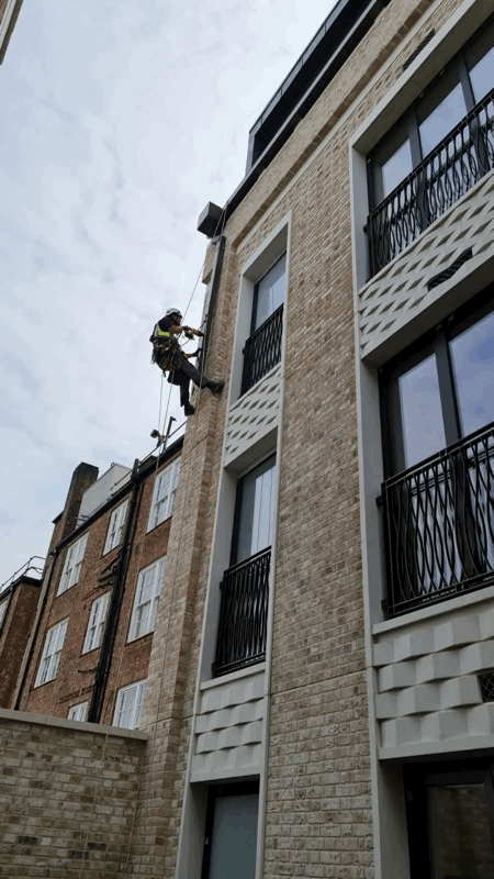 Rope Access Cladding Inspection on Residential Facade Rope access technician abseiling down a beige brick-clad apartment building to inspect the facade cladding