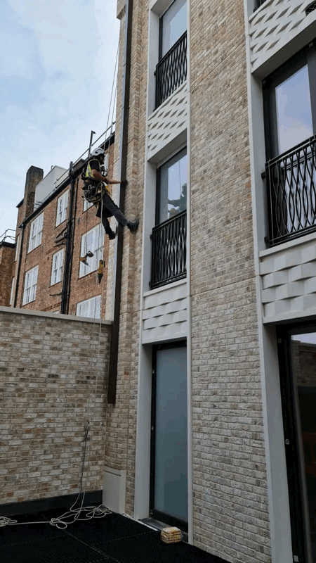 Rope access technician inspects beige brick slip cladding on a modern residential building facade.