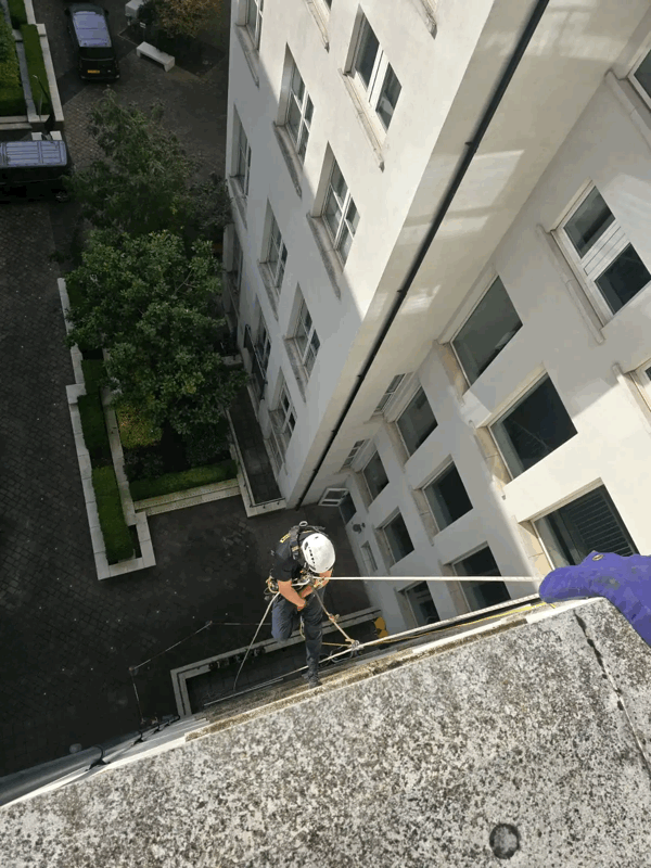Rope access technician in helmet inspects a white multi-storey building facade from height