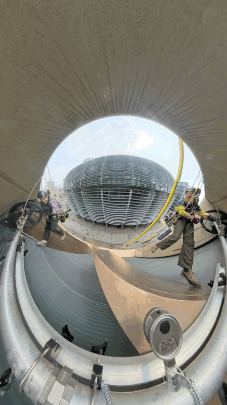 Two rope access technicians in harnesses inspect the interior of a large cylindrical flue above a domed building
