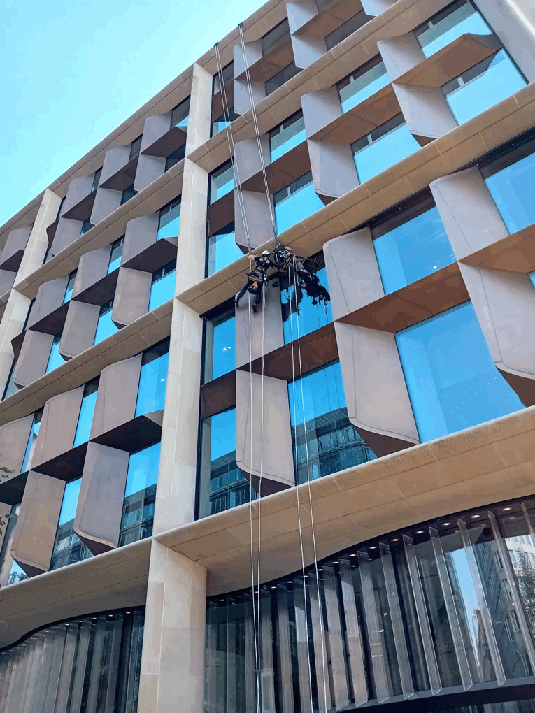 Rope access technicians inspect stone-clad facade with glass windows on a modern high-rise building