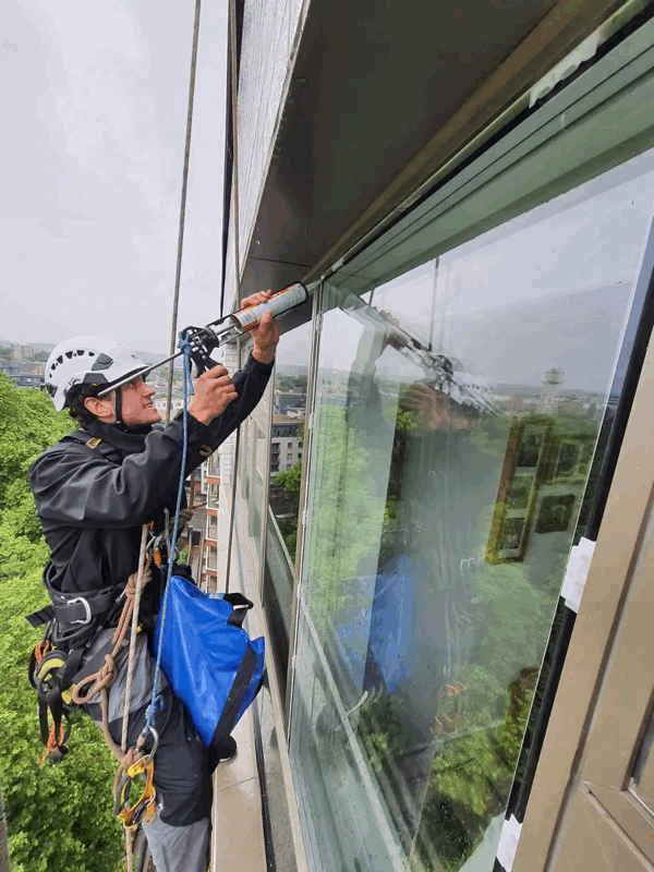 Rope access technician applying sealant around a high-rise window frame during facade maintenance