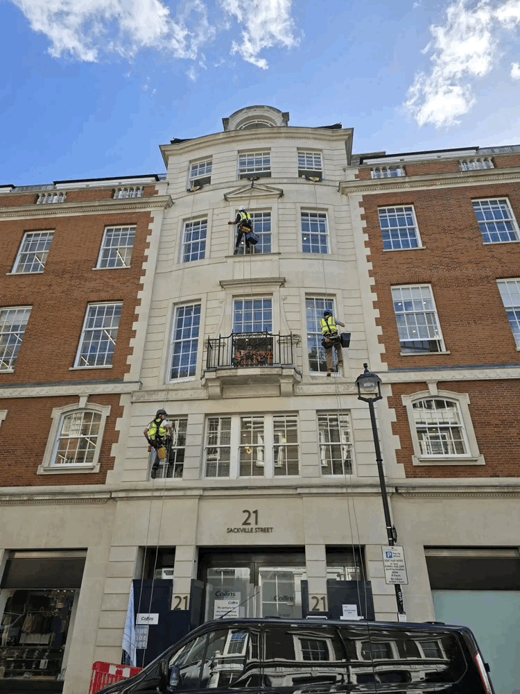 Rope access technicians in harnesses inspect the stone and brick facade of 21 Sackville Street building